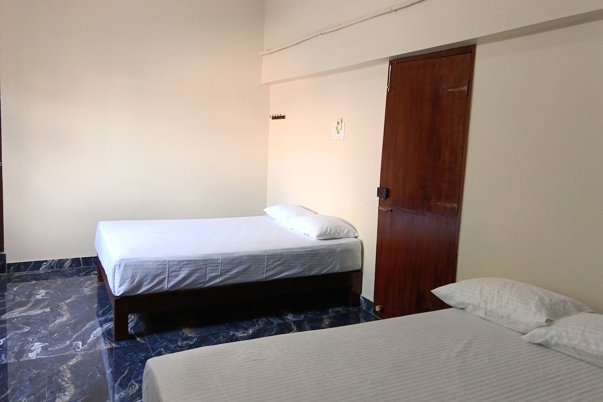 A room with two beds, a wooden door, and a marble floor.