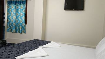 A hotel room with a bed, a flat-screen TV mounted on the wall, and a curtain with a leaf pattern.