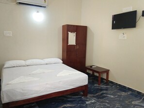 Una habitación de hotel con una cama, un armario de madera, una mesita, un televisor montado en la pared y un equipo de aire acondicionado.