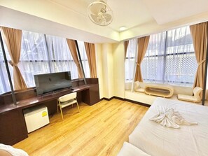 Habitació d'hotel amb un llit, una taula de treball amb televisió, una cadira i una finestra amb cortines.