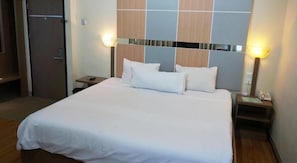 Een hotelkamer met een groot bed, twee nachtkastjes, een nachtlampje en een wandlamp.