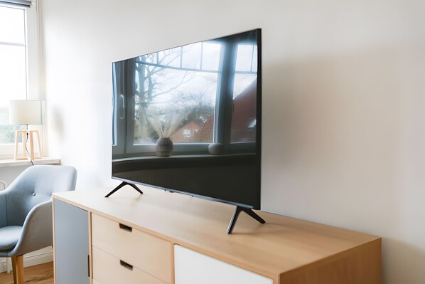 A flat-screen TV on a wooden TV stand with a window behind it.