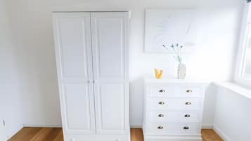 A white wardrobe with a mirror, a white dresser with drawers, and a wall-mounted artwork.