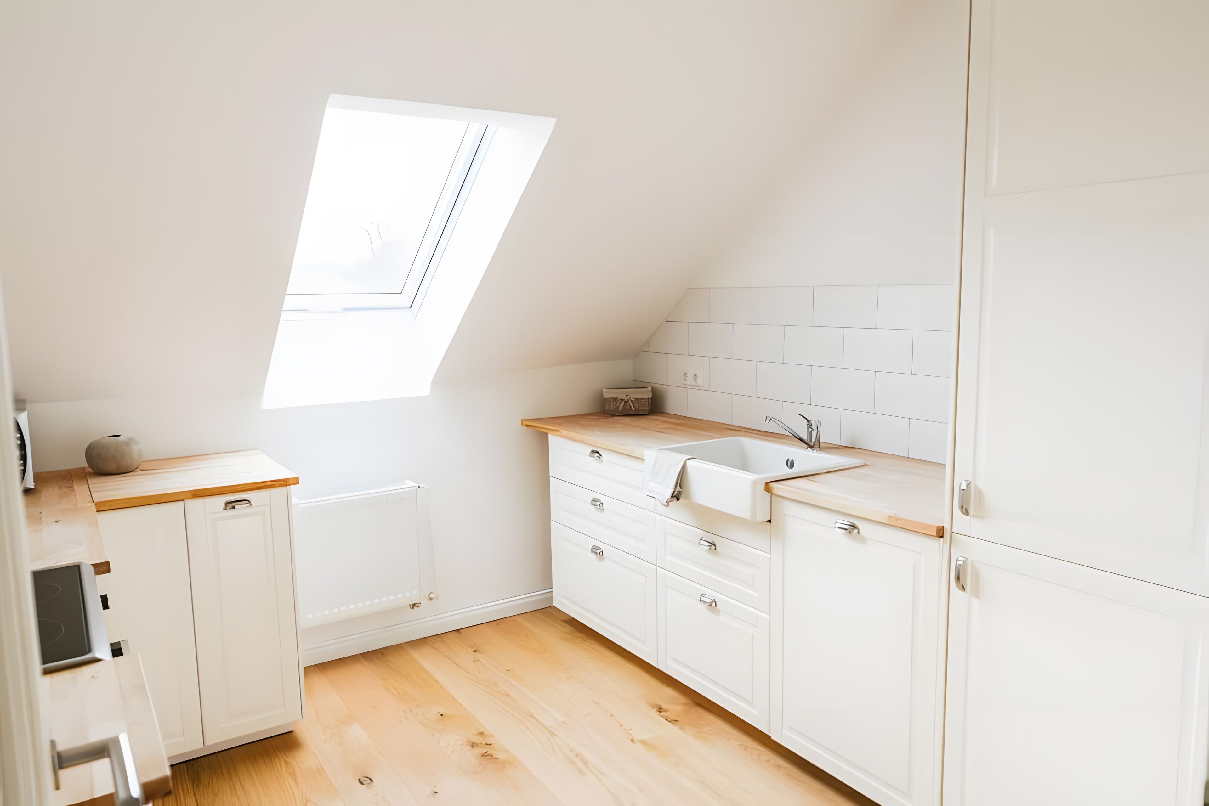 A small, white kitchen with a skylight, wooden countertop, and white cabinets.