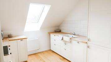 A small, white kitchen with a skylight, wooden countertop, and white cabinets.