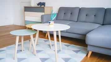A modern living room with a grey sofa, two round tables, and a geometric patterned rug.