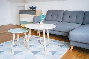 A modern living room with a grey sofa, two round tables, and a geometric patterned rug.