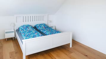 A white bed with a blue floral bedspread and matching pillows, a white nightstand with a lamp, and a wooden floor.