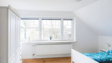 A bedroom with a white radiator, a window with blinds, a bed with a floral bedspread, and a white wardrobe.