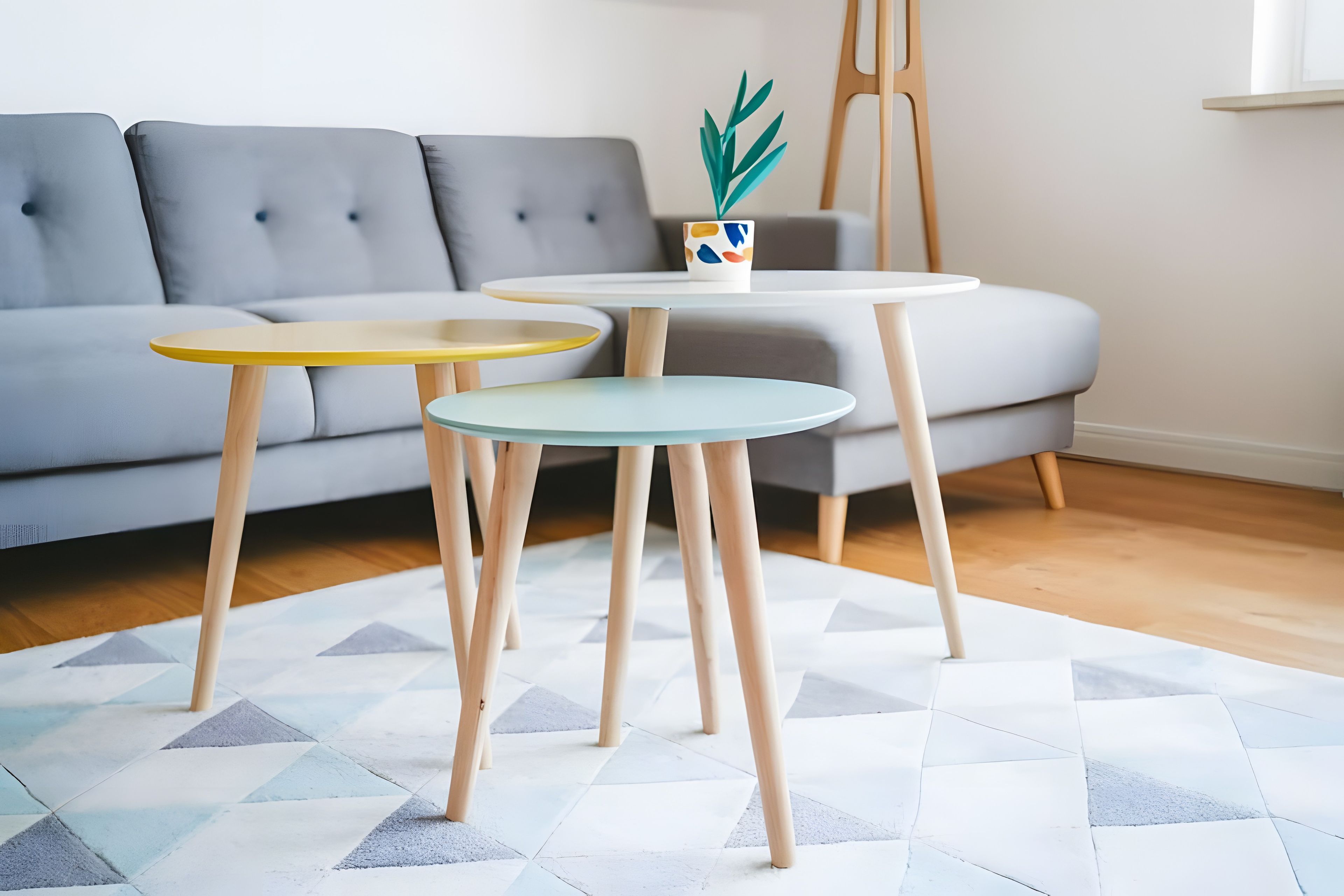 Un soggiorno moderno con un divano grigio, tre piccoli tavolini con gambe in legno e un tappeto decorato.