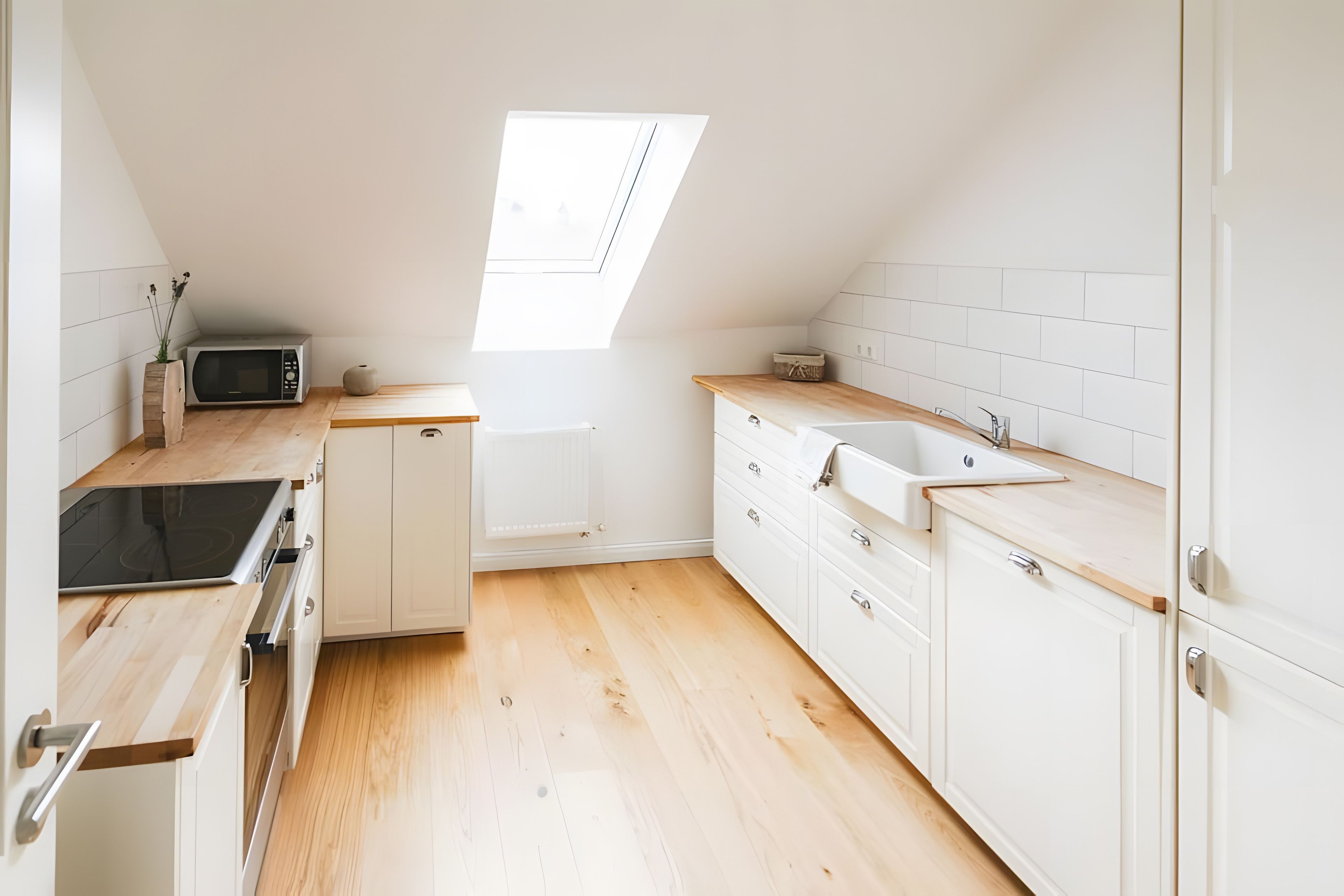 A modern kitchen with white cabinetry, a wooden countertop, a built-in microwave, and a skylight.