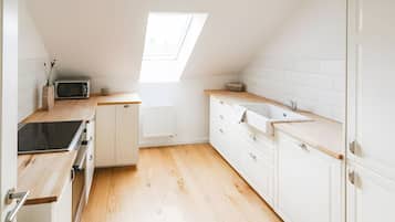 A modern kitchen with white cabinetry, a wooden countertop, a built-in microwave, and a skylight.