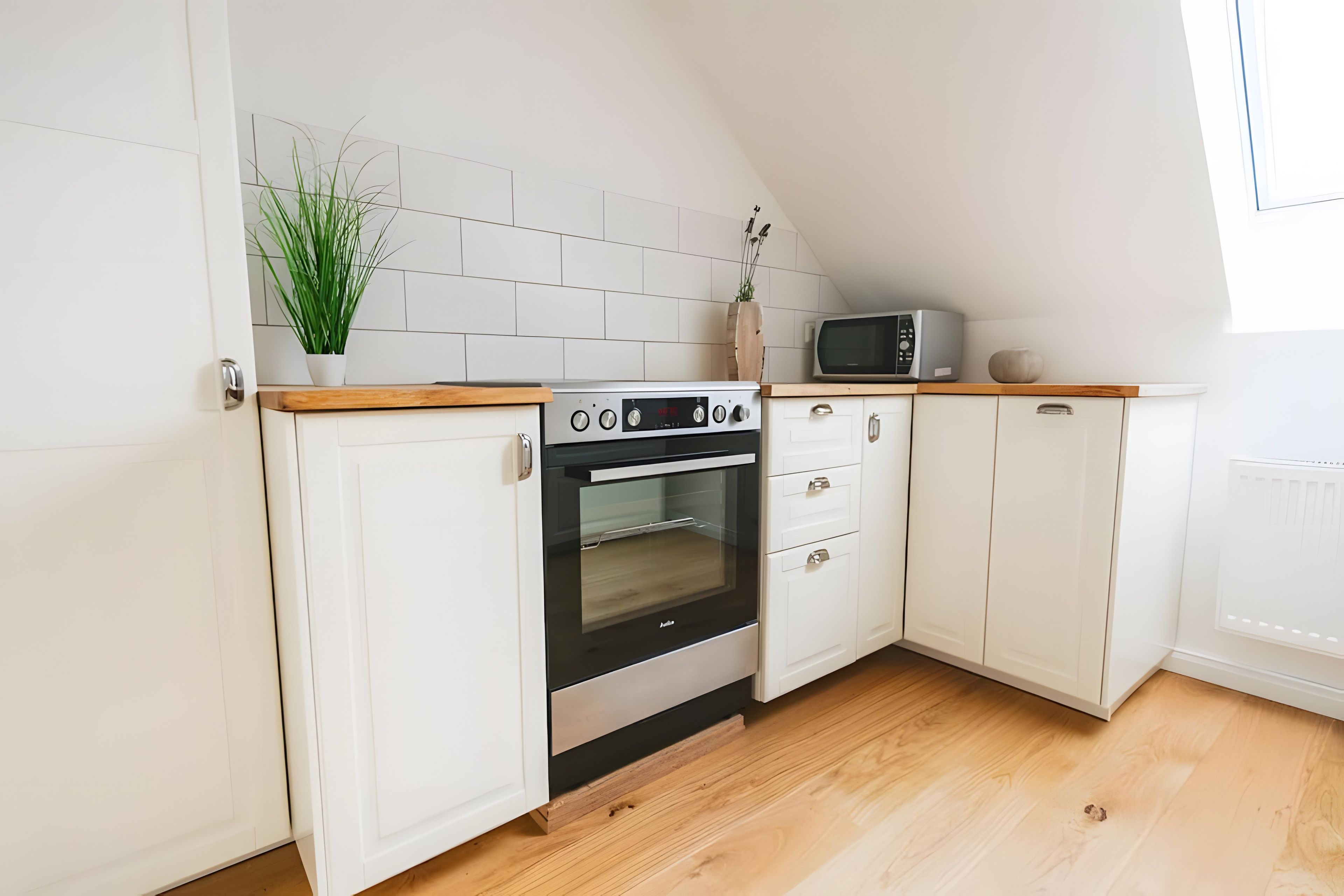 Een keuken met witte kastjes, een inbouwoven, een magnetron en een houten aanrecht.