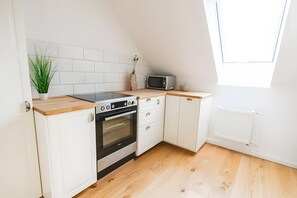 A compact kitchen with white cabinetry, a built-in oven, a microwave, and a wooden countertop.