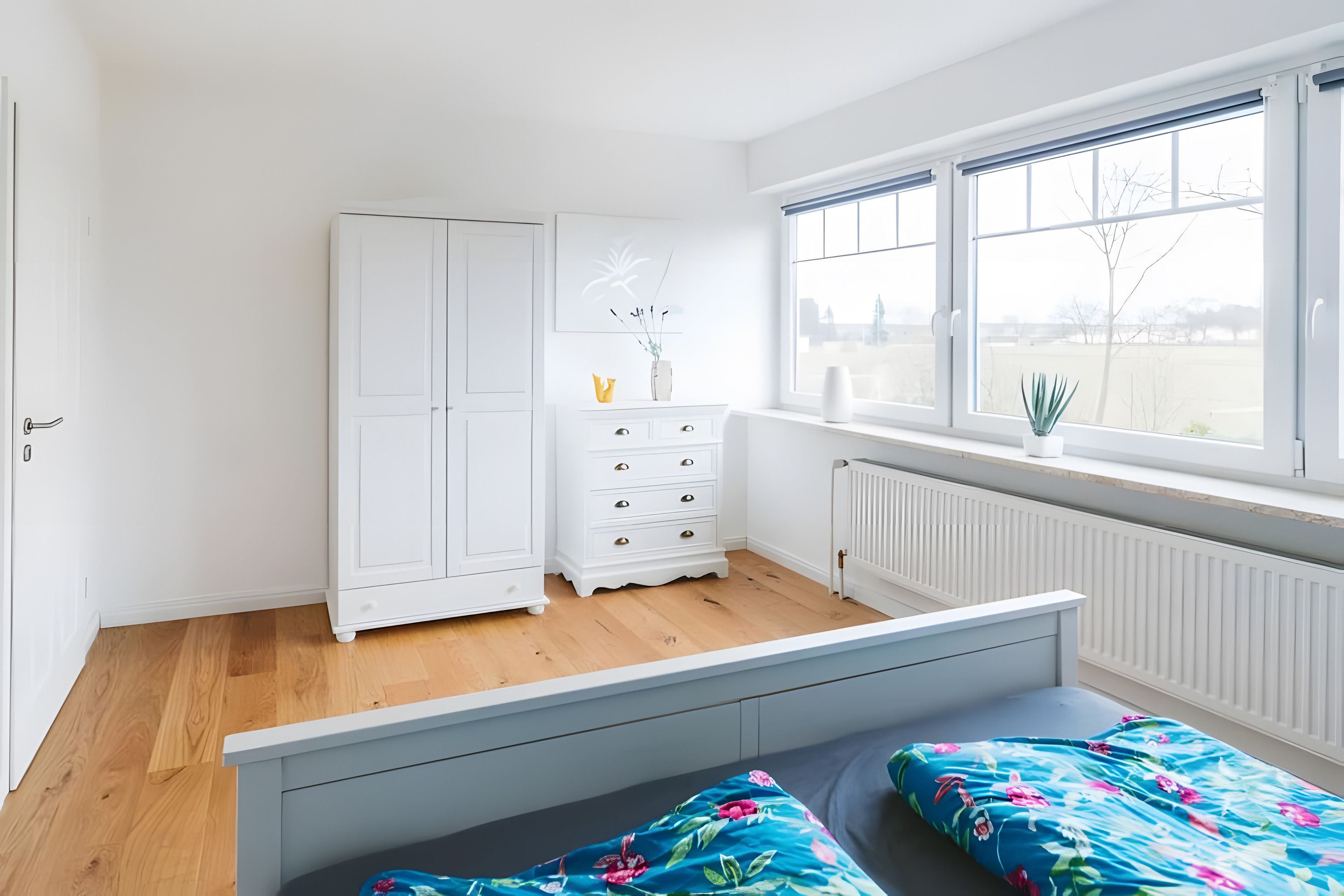 Een kamer met een bed, een dressoir, een raam met uitzicht en een radiator.