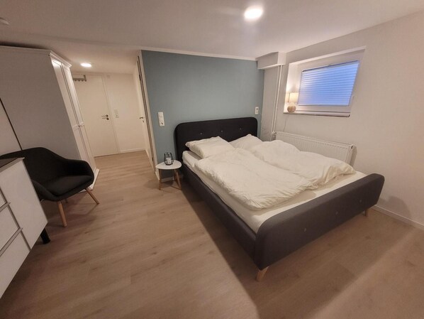 A bedroom with a bed, a chair, a small table, and a window.