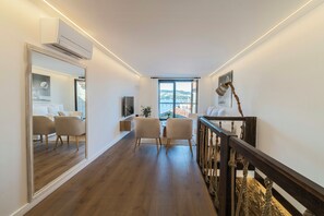 A modern hotel room with a wooden floor, a large mirror, a bed with white linens, two chairs, a TV, and a window with a view of the outdoors. - An 1800s home in Combarro's historic quarter (Pontevedra)