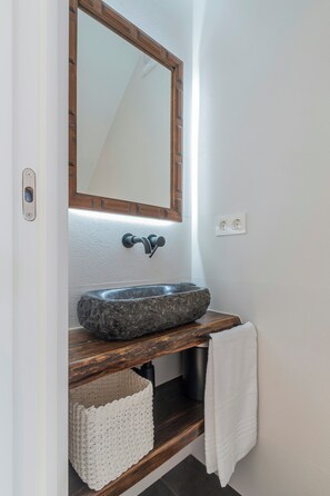 Un bagno con lavabo in pietra, mobile contenitore in legno, uno specchio e un portasciugamani.