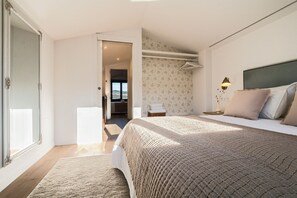 A bedroom with a large bed, a nightstand, a lamp, and a view through an open door. - An 1800s home in Combarro's historic quarter (Pontevedra)