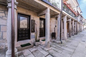 A stone building with two dark wooden doors, a stone staircase, and a balcony with potted plants. - An 1800s home in Combarro's historic quarter (Pontevedra)