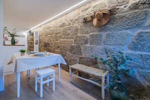 A dining area with a stone wall, a table set with plates, glasses, and cutlery, and a bench. - An 1800s home in Combarro's historic quarter (Pontevedra)