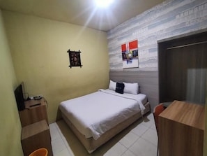 A bedroom with a bed, a desk, and a chair. There is a small table with a lamp, a wall-mounted shelf, and a door. - Hotel Bestskip Palembang (Palembang)