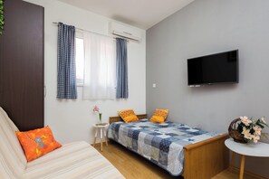 A bedroom with a bed, a TV, a small table with flowers, a window with curtains, and a sofa with a cushion. - A2 - Modern apartment with garden, 80m from beach (Vinišće)
