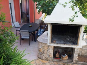 Eine Terrassenanlage mit einem Grill aus Stein, einem runden Tisch und Stühlen.