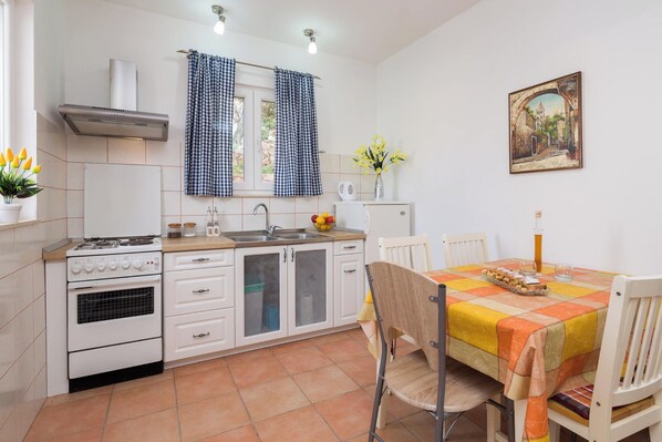 Een keuken met witte kastjes, een fornuis en een eettafel met een geruit tafelkleed.