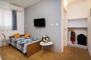 Een slaapkamer met een bed, een televisie, een kleine tafel met een vaas, een kledingkast en een koffer.