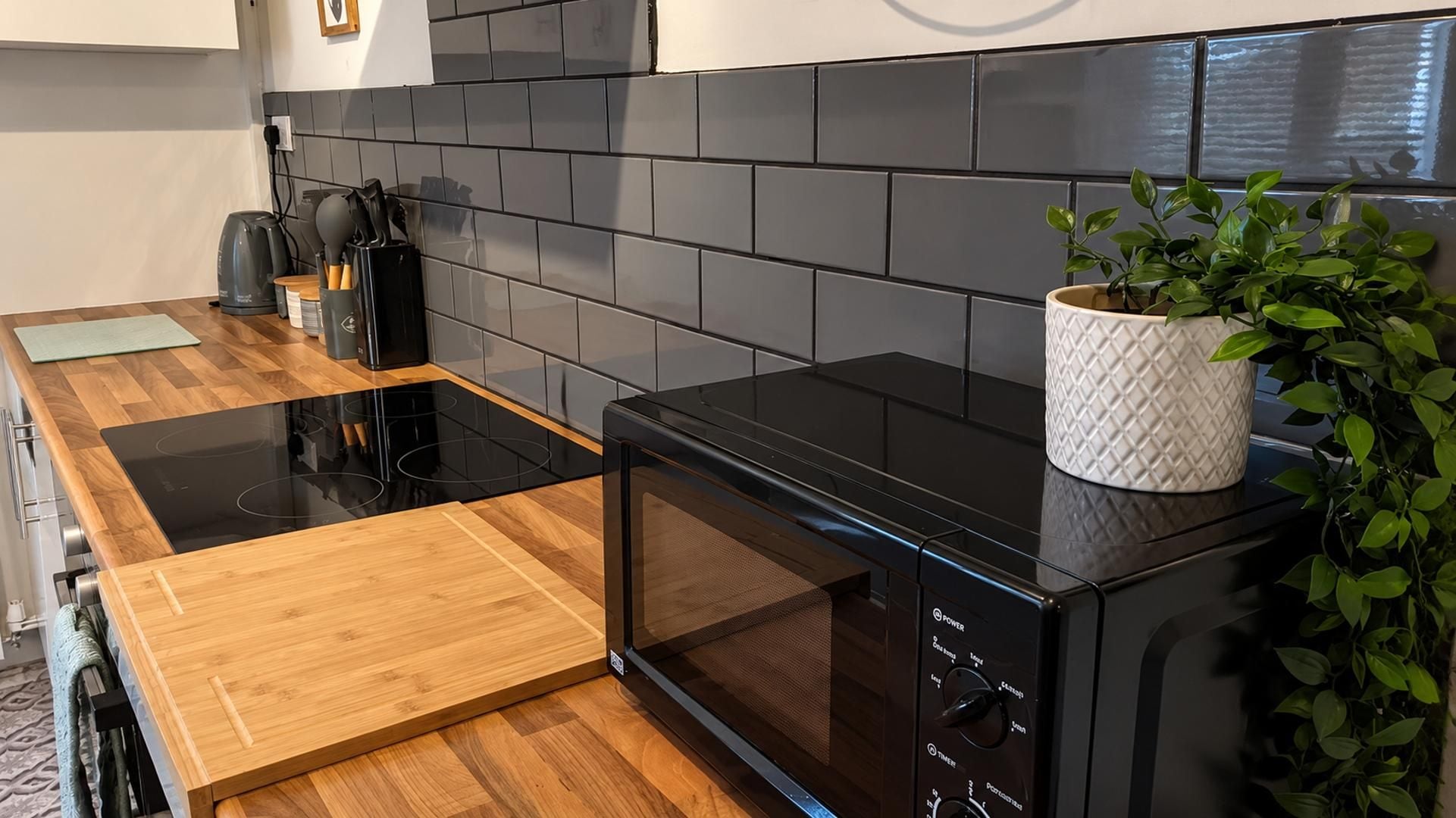 A modern kitchen with a black microwave, wooden countertop, and a potted plant.