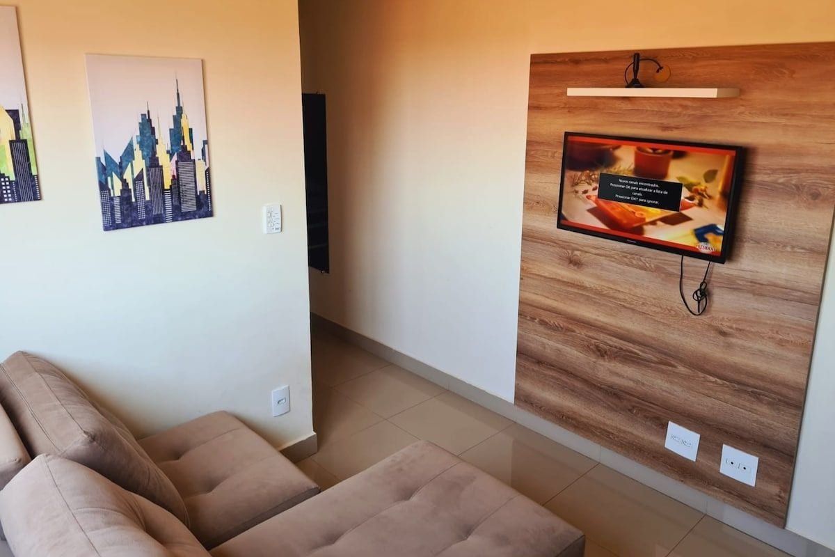 Un soggiorno moderno con un divano, una televisione fissata a una parete in legno e due opere d'arte raffiguranti paesaggi urbani.