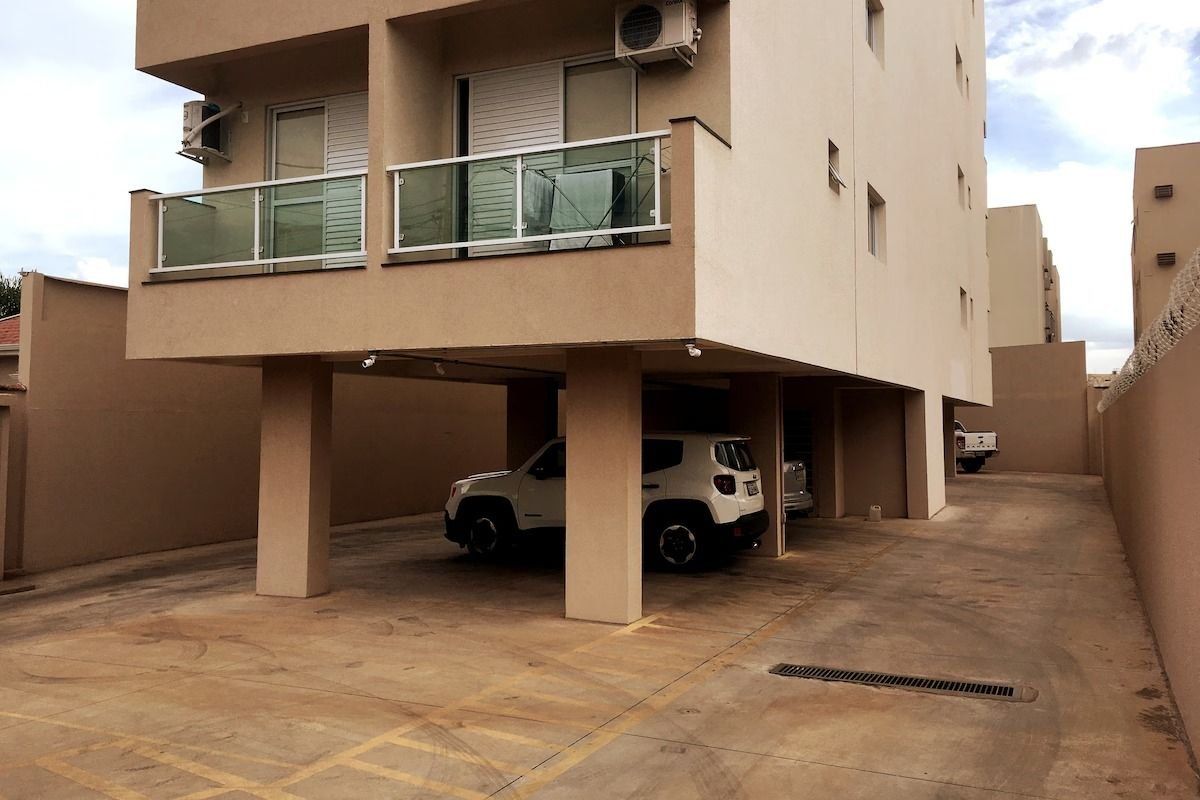 Edifício residencial com vários andares, área de estacionamento coberta e um SUV branco estacionado no interior.