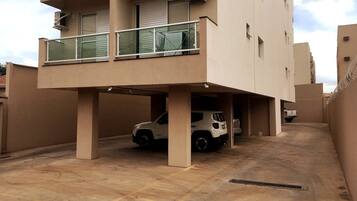 Edifício residencial com vários andares, área de estacionamento coberta e um SUV branco estacionado no interior.