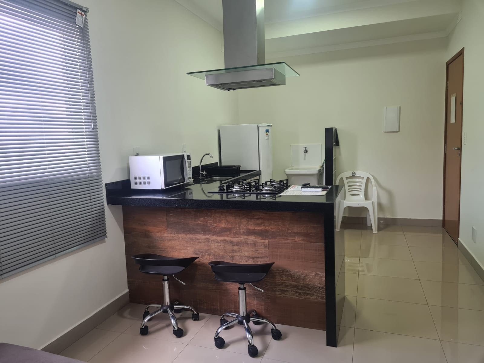 A compact kitchen with a microwave, gas stove, and a small refrigerator. There are two stools at the counter.