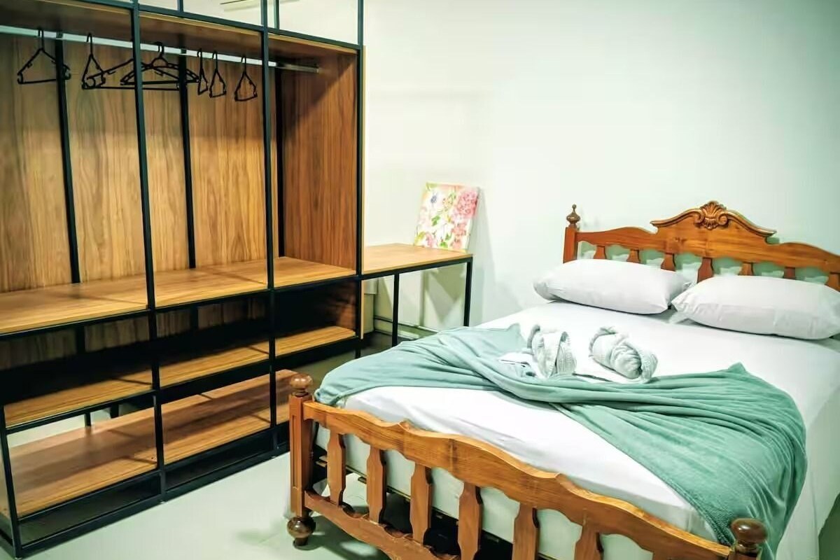 A bedroom with a wooden bed, a wooden wardrobe, and a wall-mounted shelf.