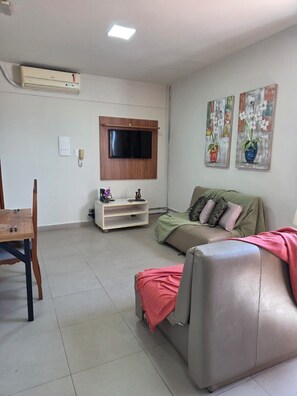 A living room with a flat-screen TV mounted on the wall, a sofa, a coffee table, and a small wooden table with a chair.