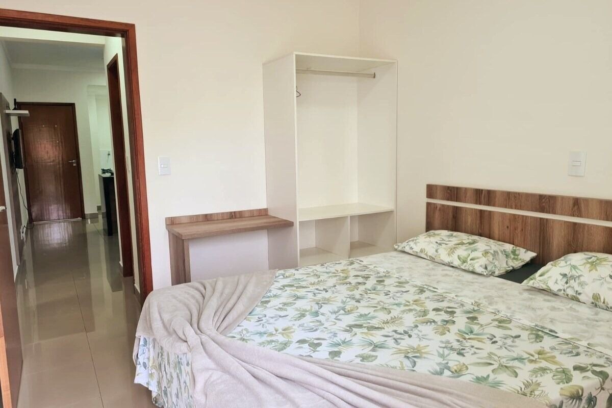 A bedroom with a bed, a bedside table, a wardrobe, and a door leading to a hallway.