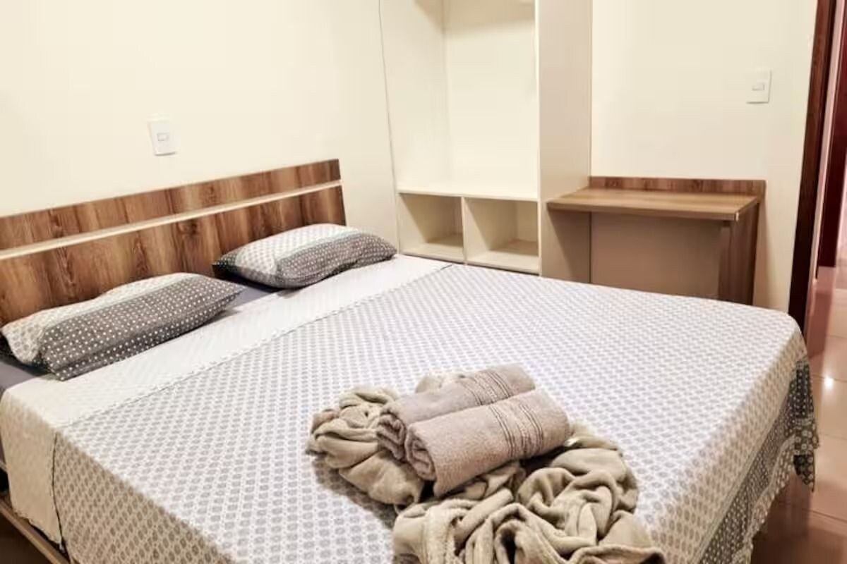 A bed with a patterned bedspread, pillows, and a rolled-up blanket.