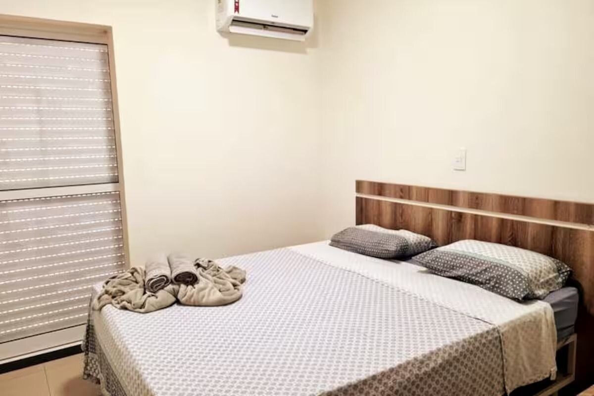 A bedroom with a bed, pillows, a blanket, and an air conditioning unit.