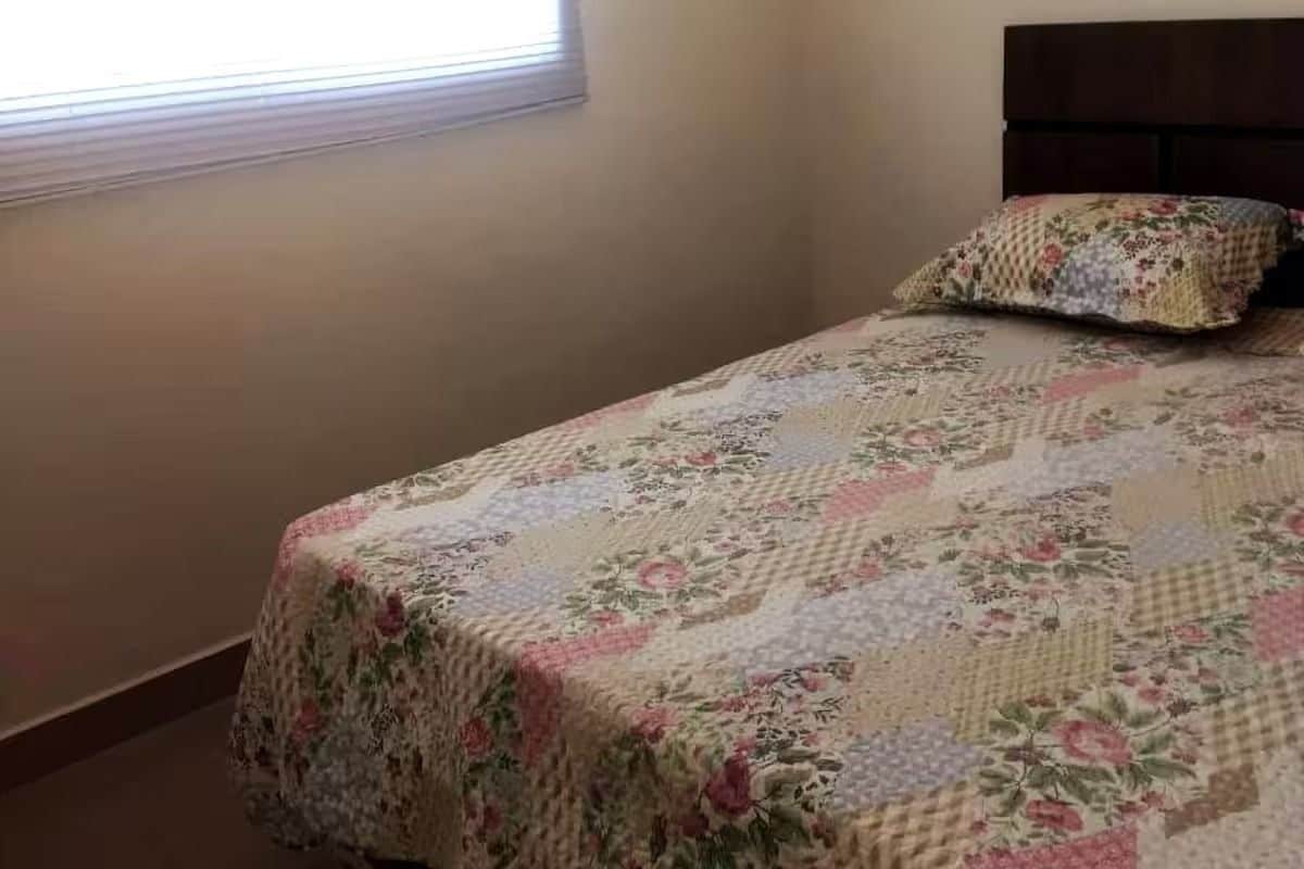 A bedroom with a bed covered in a floral-patterned quilt, a matching pillow, and a window with blinds.