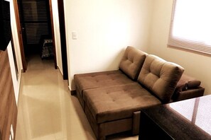 A compact living space with a sofa, a small table, and a window with blinds. - EdifÃcio 1125 (São José do Rio Preto)