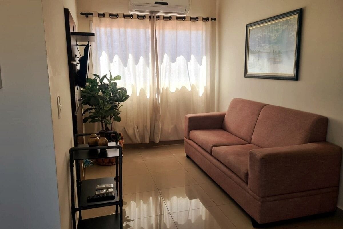 A living room with a sofa, a potted plant, a TV stand, and a framed picture on the wall.