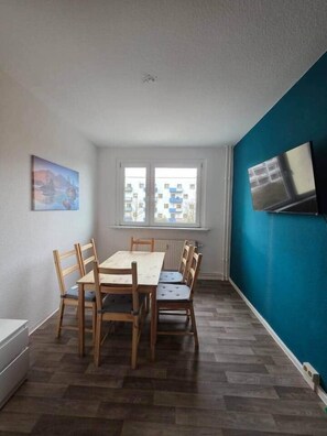 Ein Essbereich mit Tisch und Stühlen, ein Fenster mit Ausblick und ein an der Wand befestigter Flachbildfernseher.