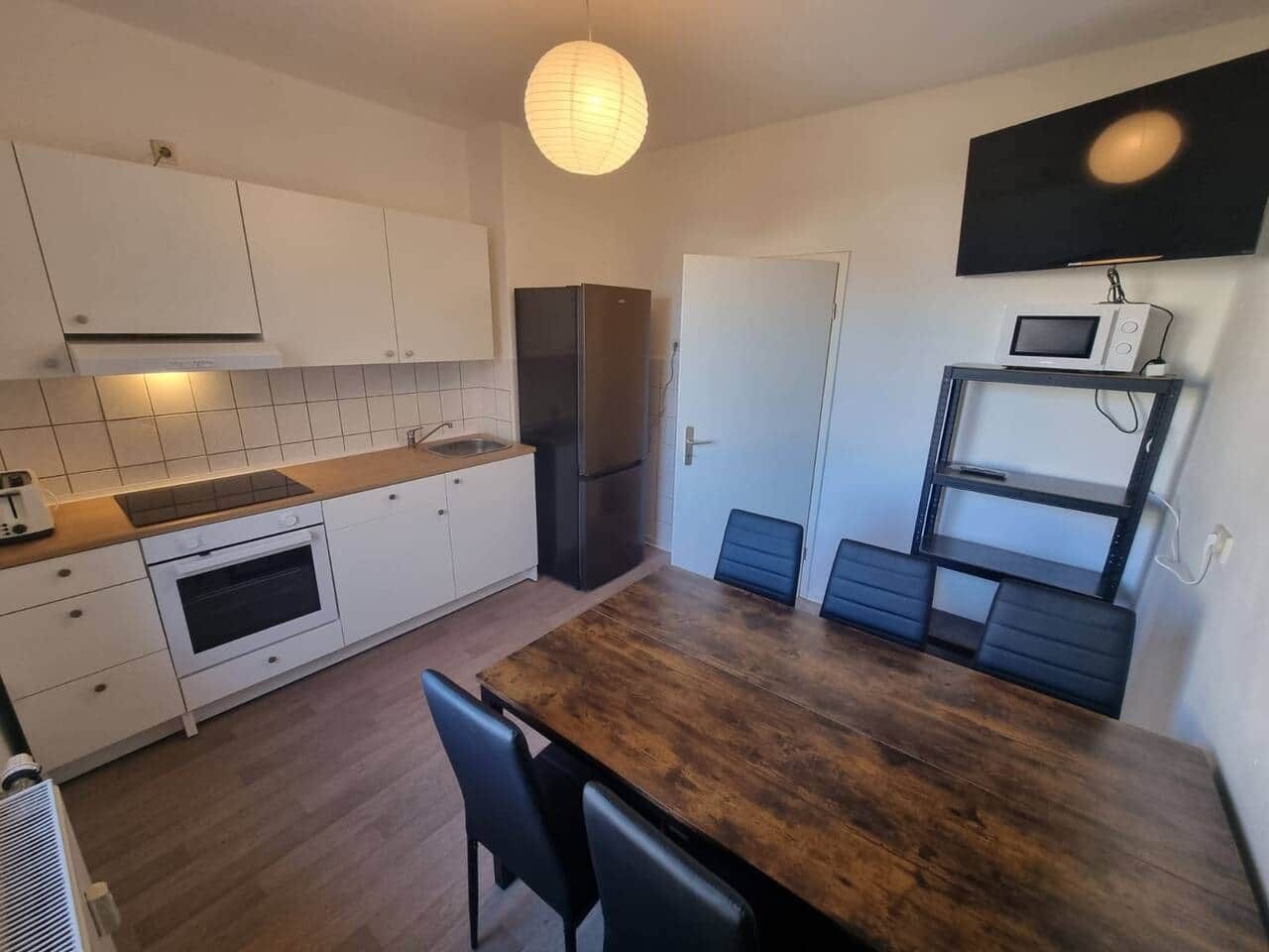 Eine kompakte Küche mit weißen Schränken, einem Holztisch und einem eingebauten Mikrowellenregal.
