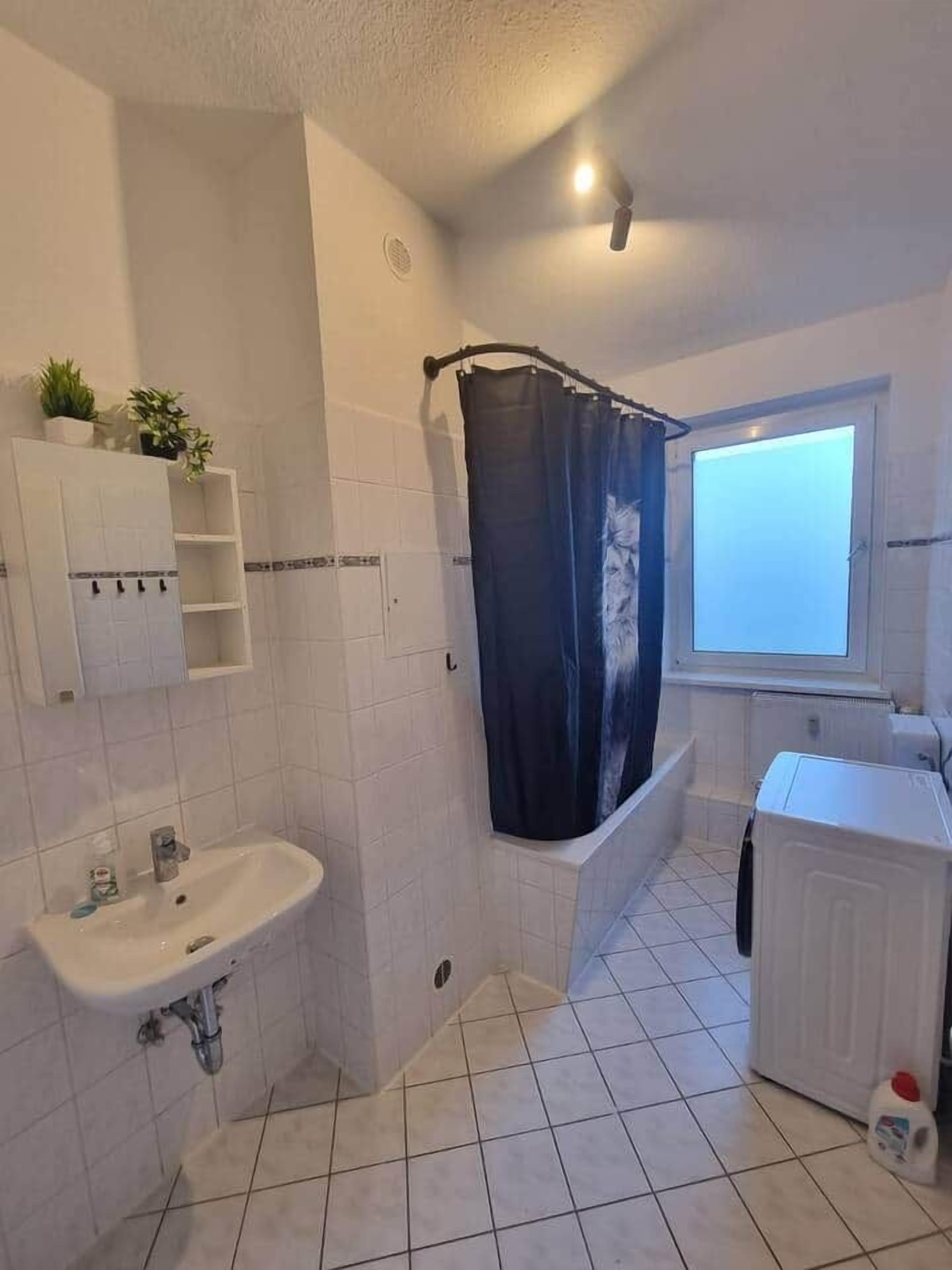 Ein Badezimmer mit Waschbecken, Duschvorhang, Fenster und Waschmaschine.