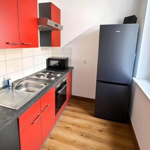 Eine kleine Küche mit roten Schränken, einem schwarzen Kühlschrank und einer Mikrowelle.