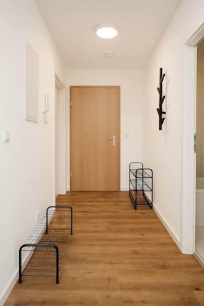 Ein Korridor mit Holzboden, einer Tür am Ende und einem Metallregal an der Wand.