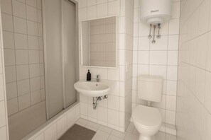 Ein Badezimmer mit weißem Waschbecken, einem Spiegel, einer Toilette und einer Duschkabine.