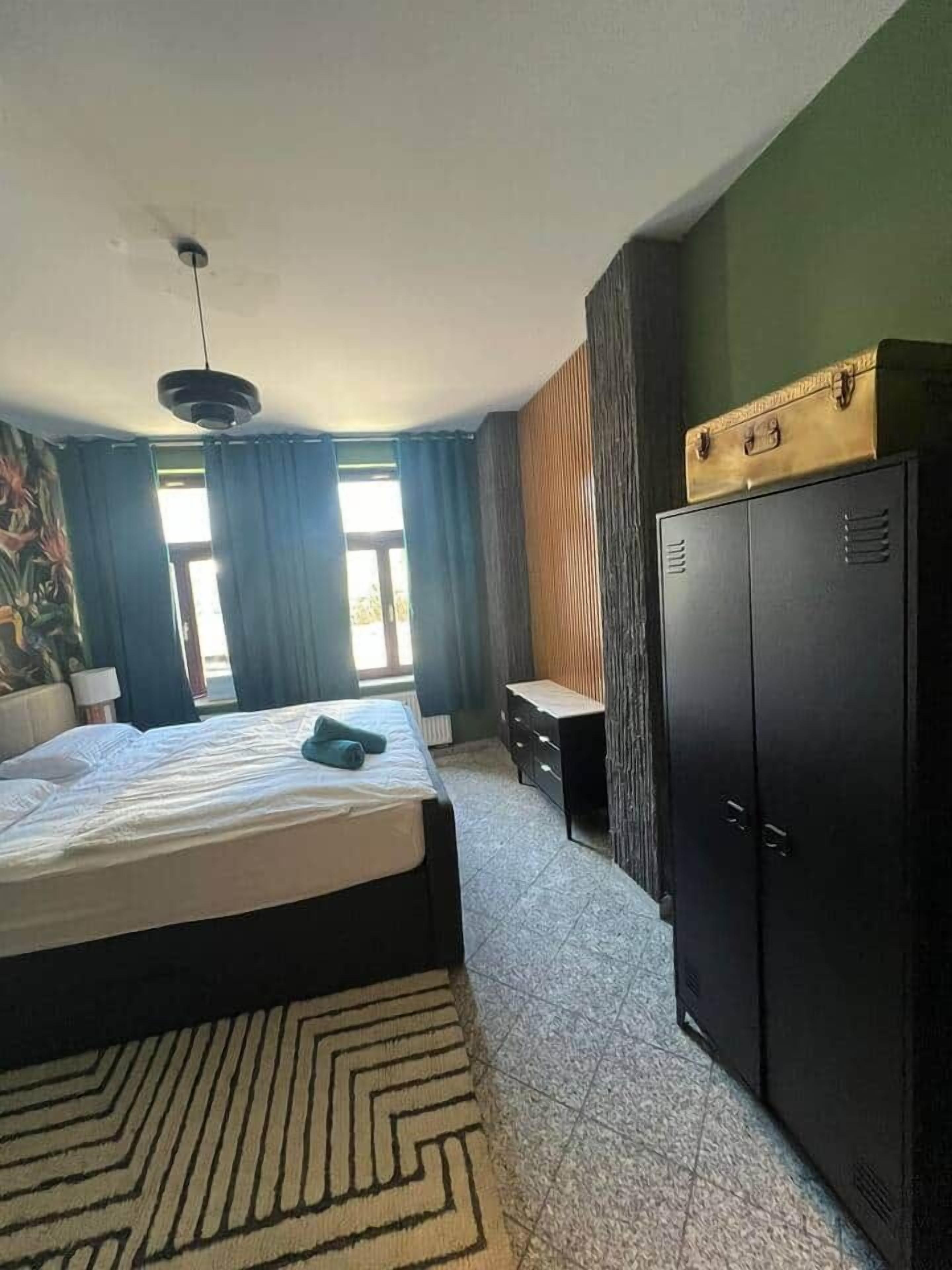 A hotel room with a bed, a desk, a wardrobe, and a window with curtains.